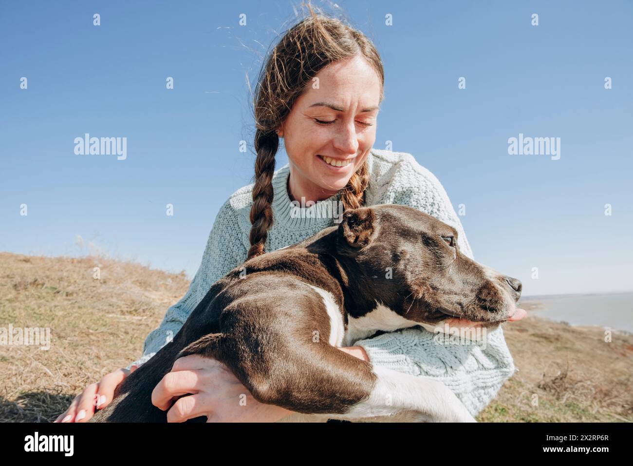 Donna sorridente che passa il tempo libero con il cane in collina durante la giornata di sole Foto Stock