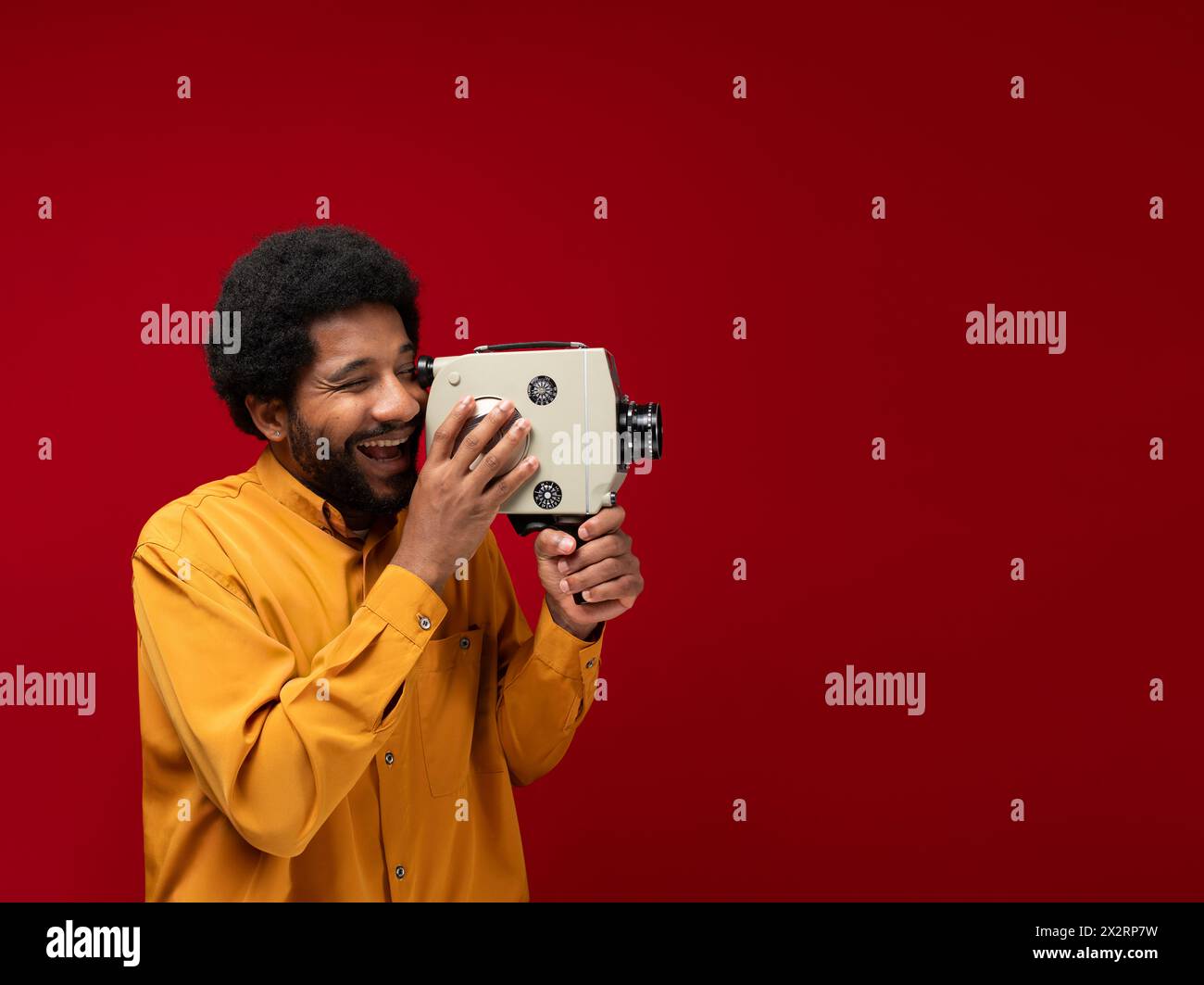 Uomo felice che guarda attraverso una videocamera d'epoca su sfondo rosso Foto Stock