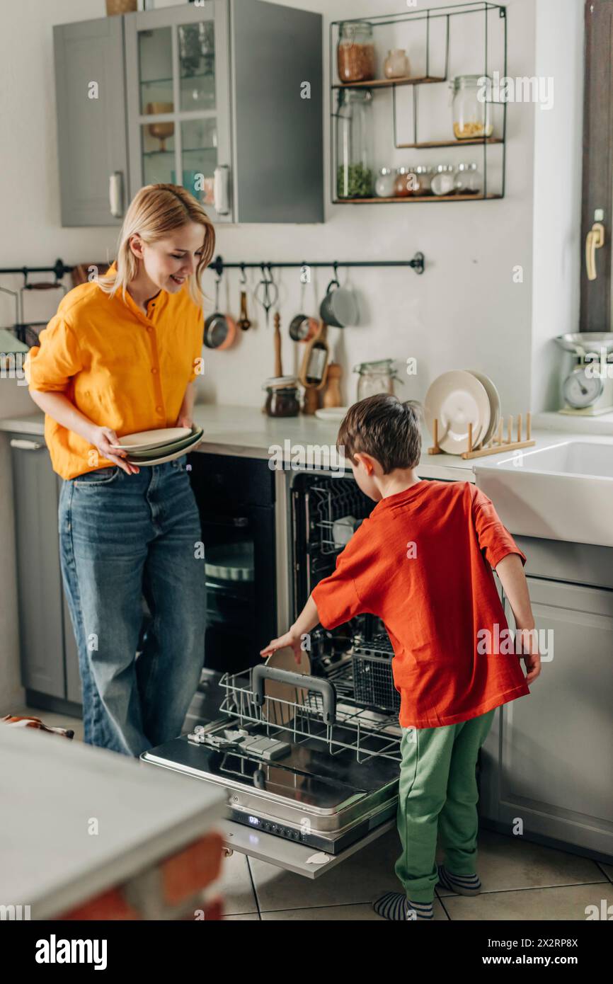 Figlio che aiuta la madre a lavare i piatti a casa Foto Stock