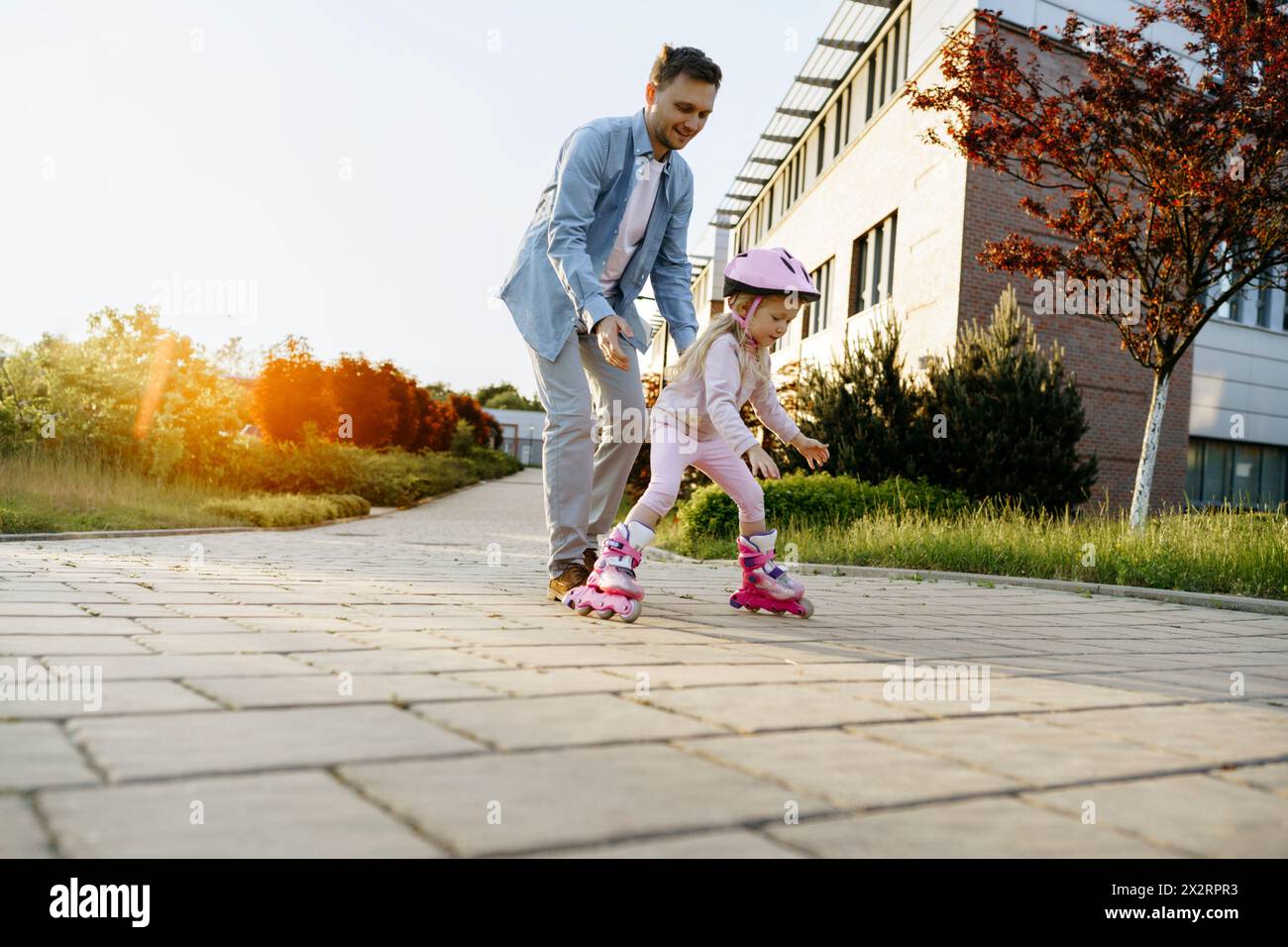 Padre che assiste la figlia pattinando sul sentiero Foto Stock