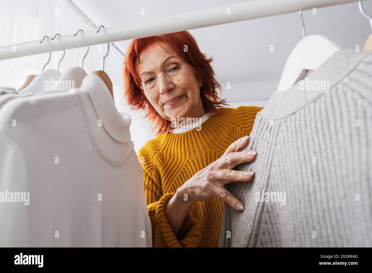 Donna anziana con i top appesi su scaffale nell'armadio Foto Stock