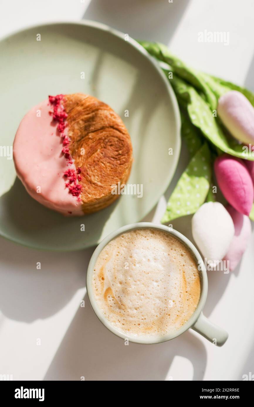 Tazza di croissant al caffè con cioccolato rosa e lamponi liofilizzati sul tavolo Foto Stock