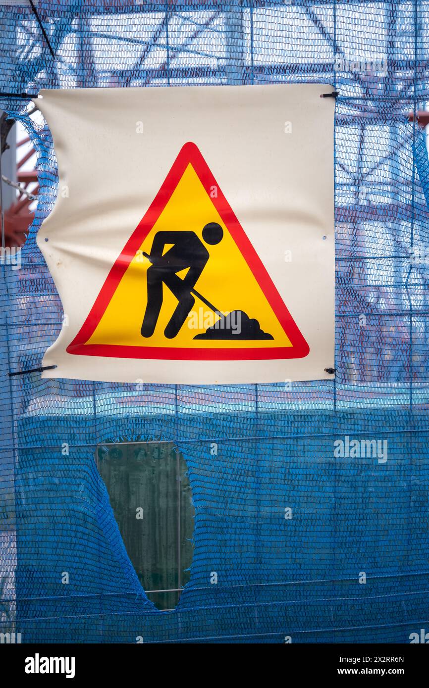 Cartello di attenzione per lavori di costruzione su una recinzione con materiali e travi sullo sfondo. Foto Stock