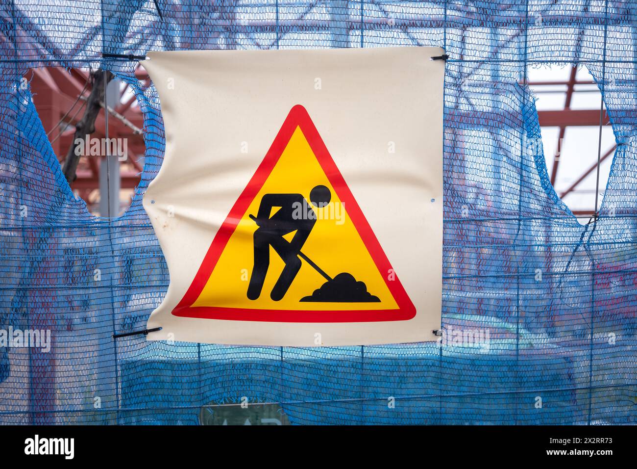Cartello di attenzione per lavori di costruzione su una recinzione con materiali e travi sullo sfondo. Foto Stock