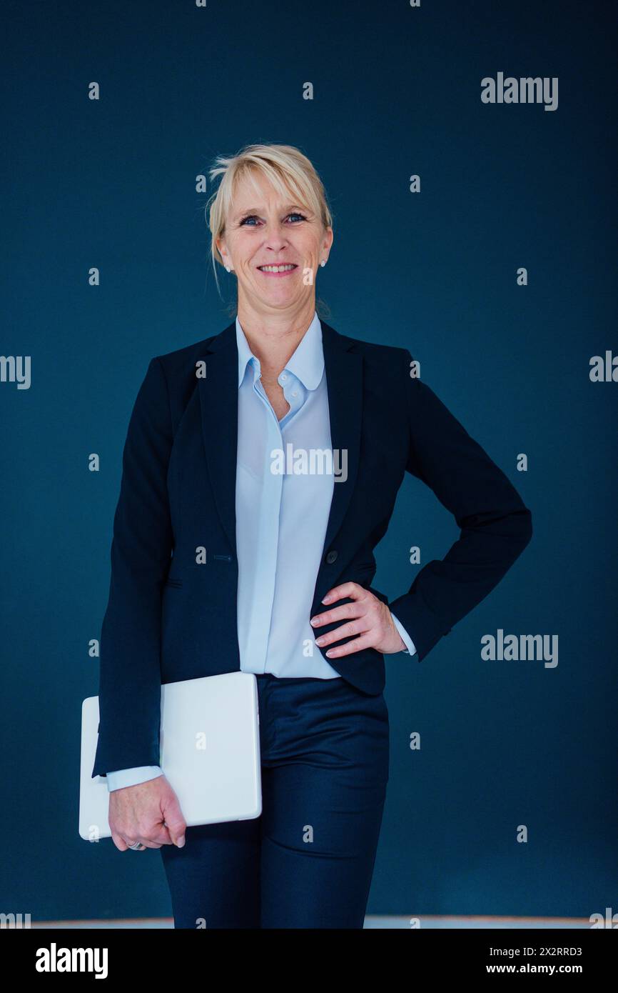 Donna d'affari felice in piedi con un notebook su sfondo blu navy Foto Stock