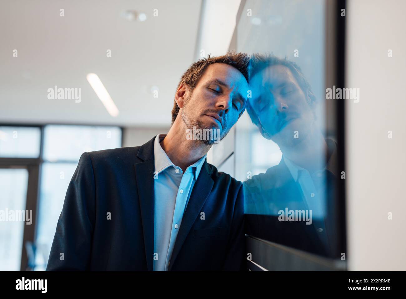 Uomo d'affari appoggiato allo schermo del computer con gli occhi chiusi in ufficio Foto Stock