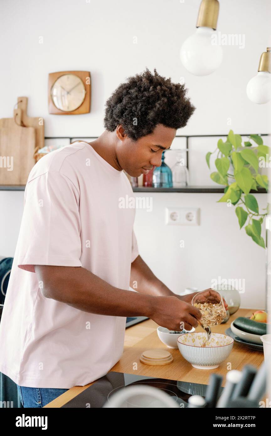 Uomo che prepara muesli per la colazione nella ciotola al bancone della cucina Foto Stock