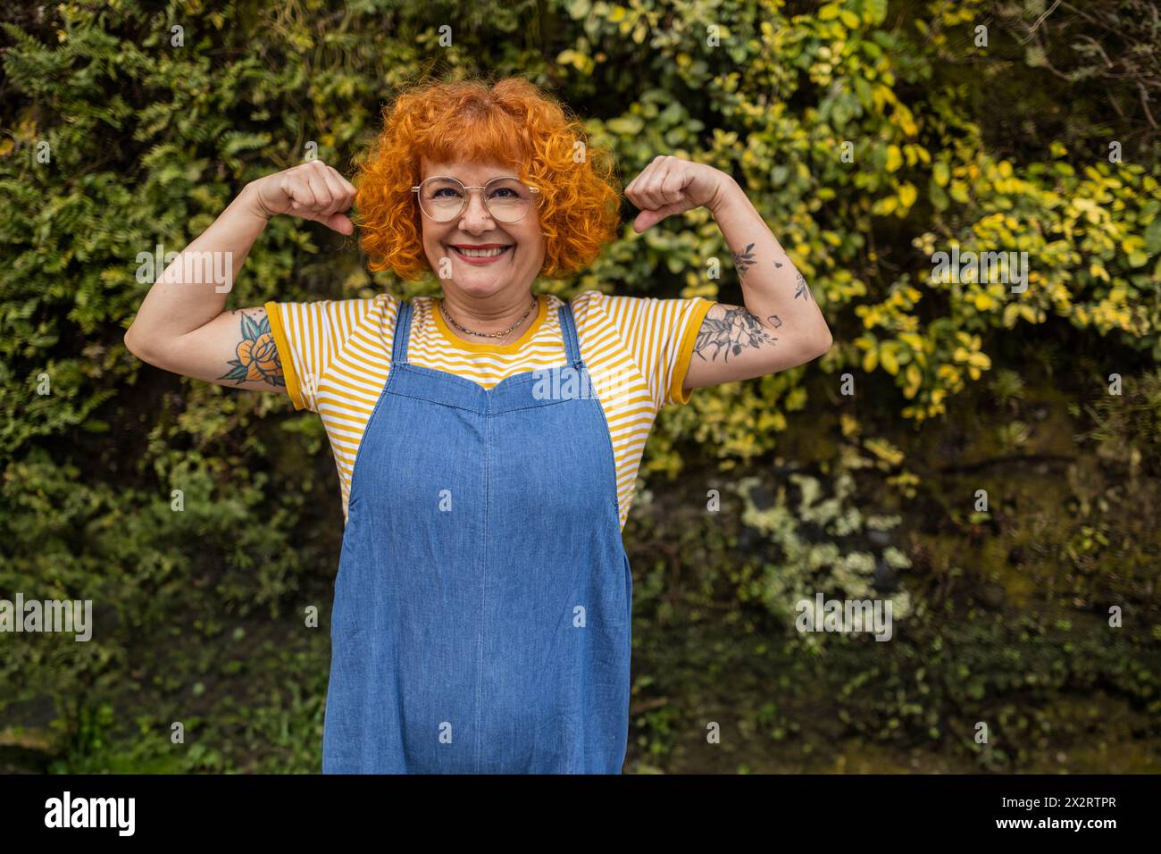 Sorridente rossa donna anziana che flessa i muscoli Foto Stock