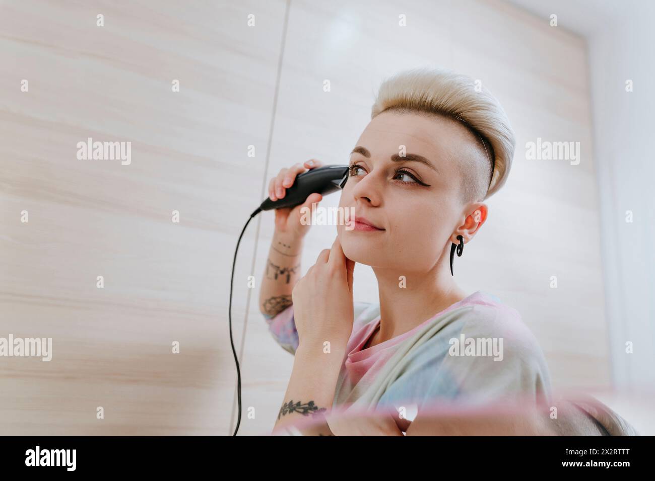 Donna hipster che rifinisce i capelli utilizzando un rasoio elettrico a casa Foto Stock
