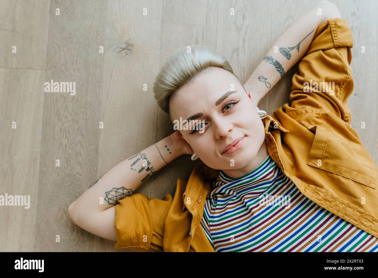 Donna sorridente con tatuaggi sdraiati sul pavimento di casa Foto Stock