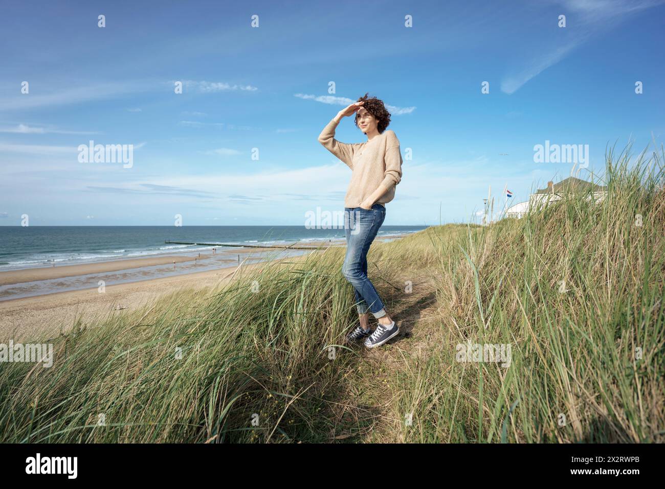 Donna che protegge gli occhi in mezzo all'erba verde in spiaggia Foto Stock