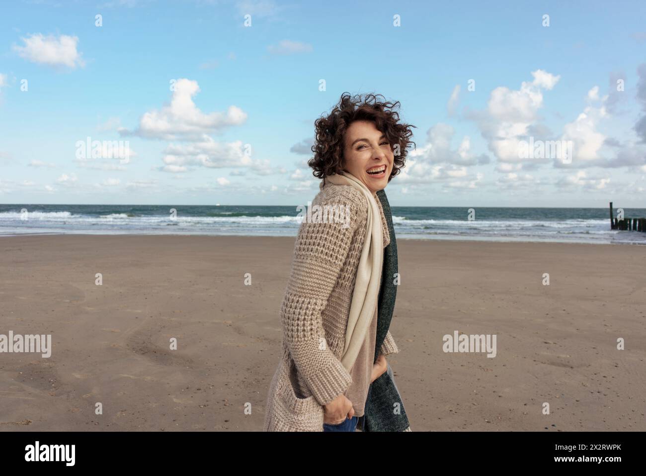 Donna allegra in maglione cardigan in piedi in spiaggia Foto Stock