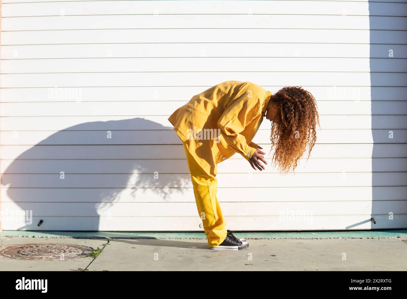 Giovane donna in giallo con capelli ricci piegati in avanti da un otturatore bianco Foto Stock
