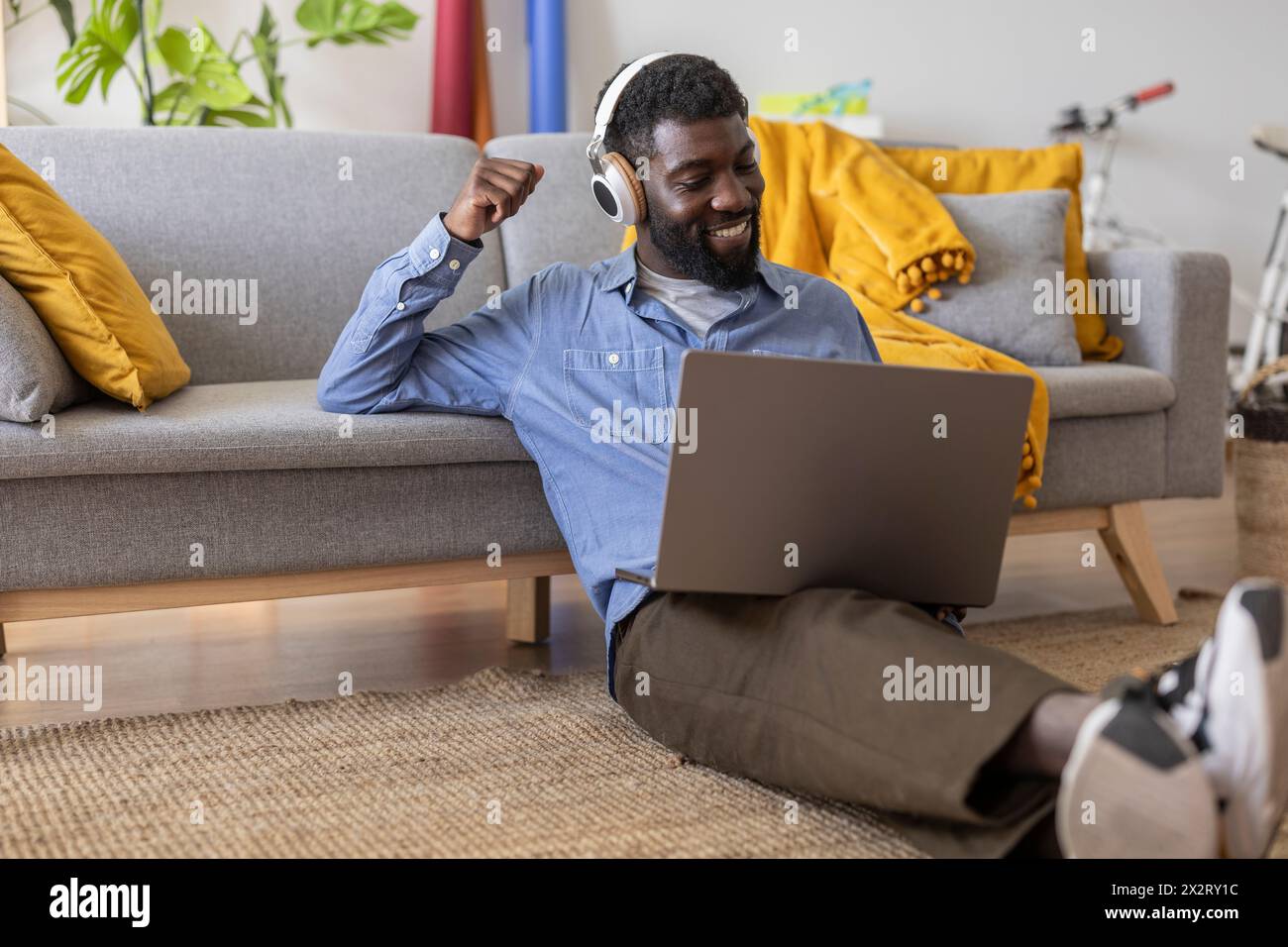 Persona sorridente che indossa le cuffie wireless e utilizza il computer portatile nel salotto di casa Foto Stock