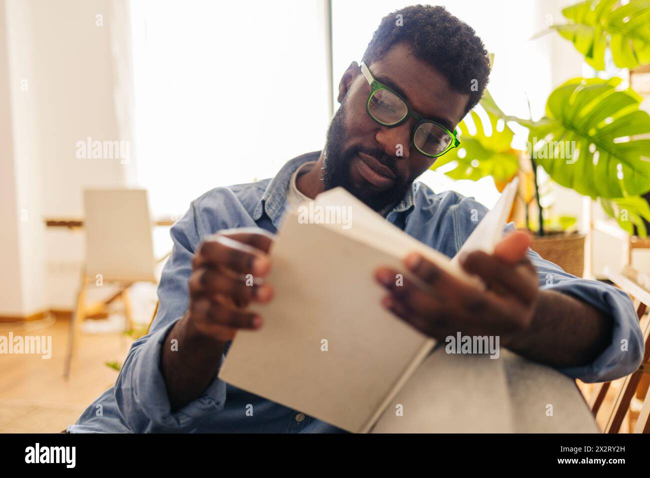 Persona non binaria che legge un libro nel soggiorno di casa Foto Stock