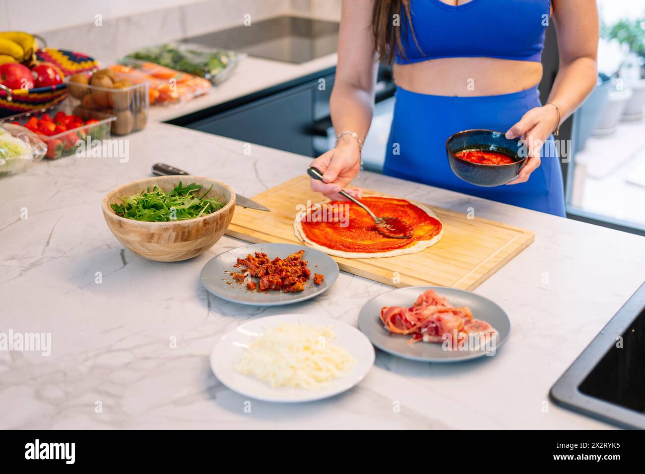 Donna che applica la salsa sulla base della pizza in cucina a casa Foto Stock