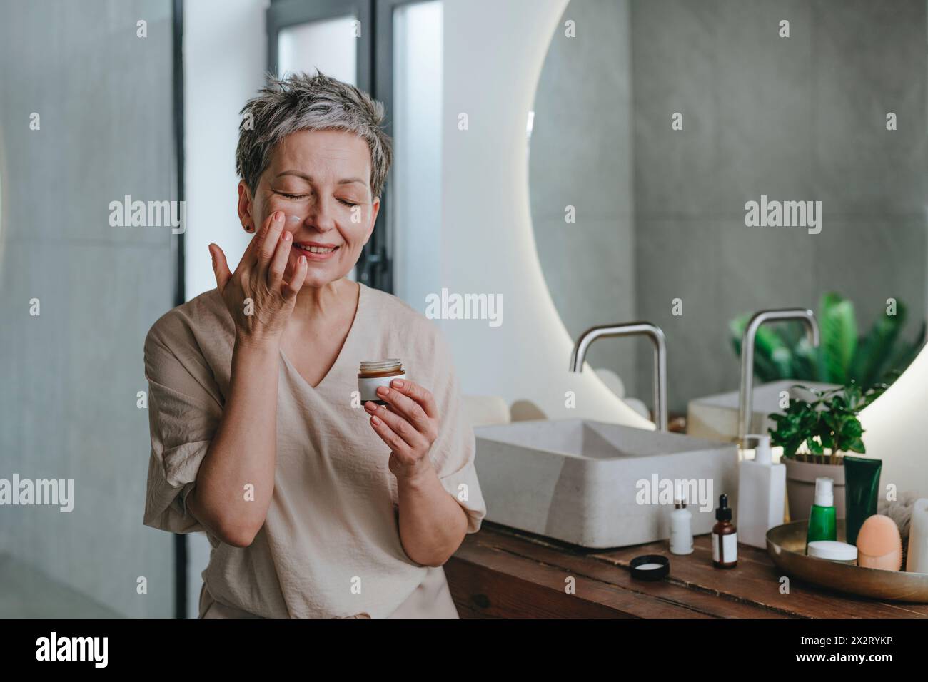 Donna che applica crema per il viso in bagno a casa Foto Stock