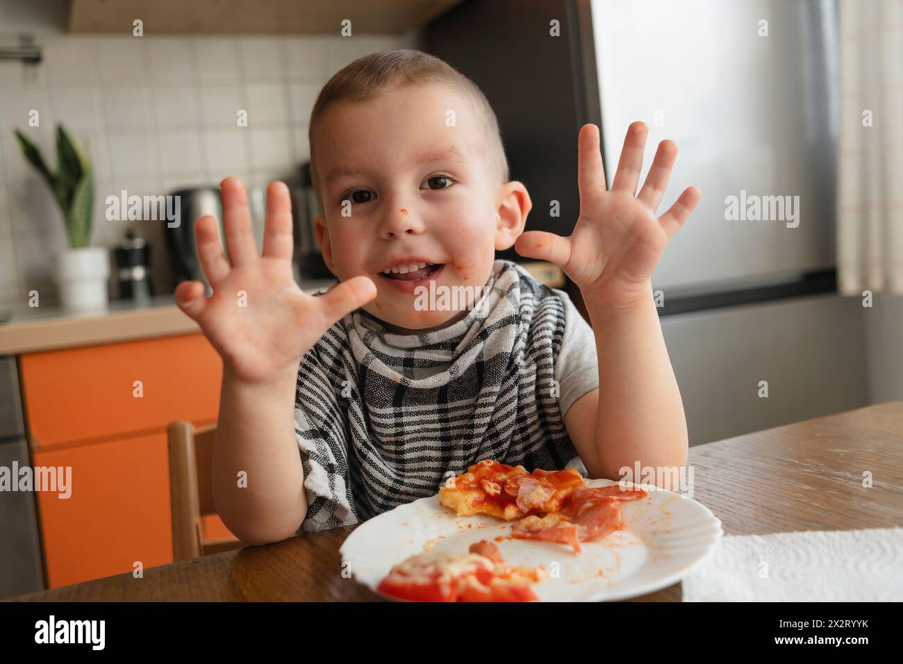 Ragazzo felice che mostra le mani vicino alla pizza a tavola in cucina Foto Stock