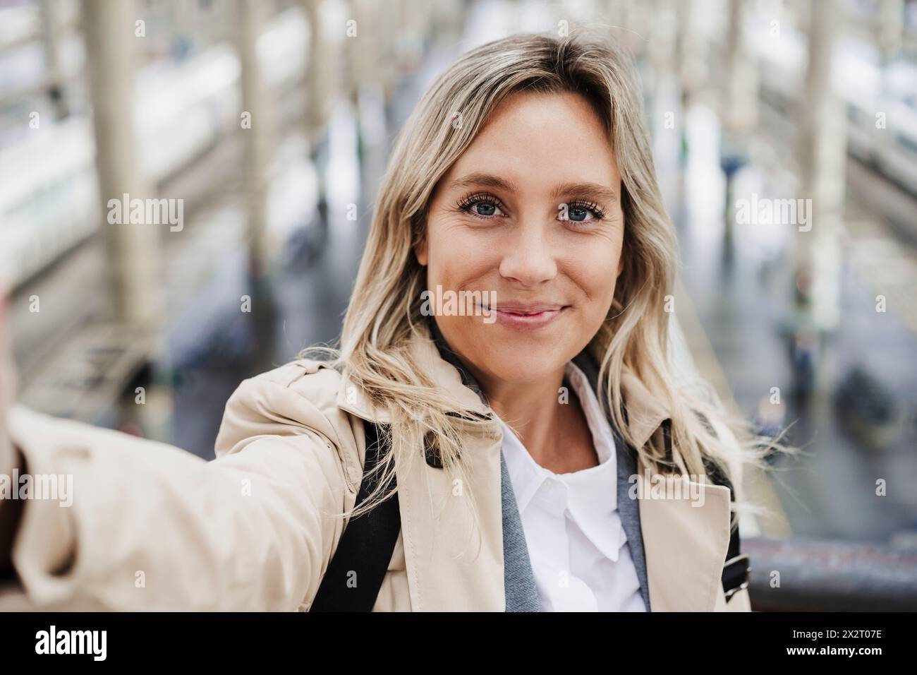Donna sorridente con capelli evidenziati che scatta selfie alla stazione ferroviaria Foto Stock
