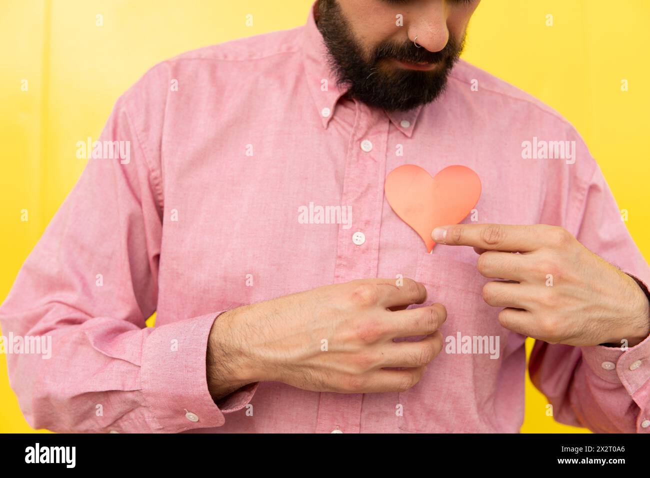 Uomo con cuore rosso su camicia rosa su sfondo giallo Foto Stock