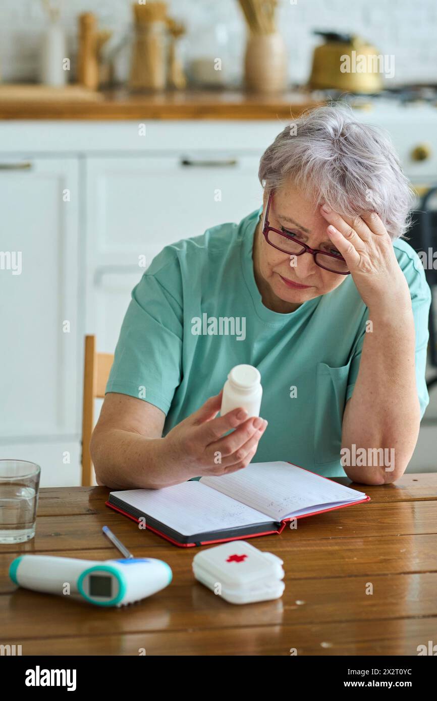 Donna preoccupata con la testa in mano che tiene a casa una bottiglia di medicinali Foto Stock