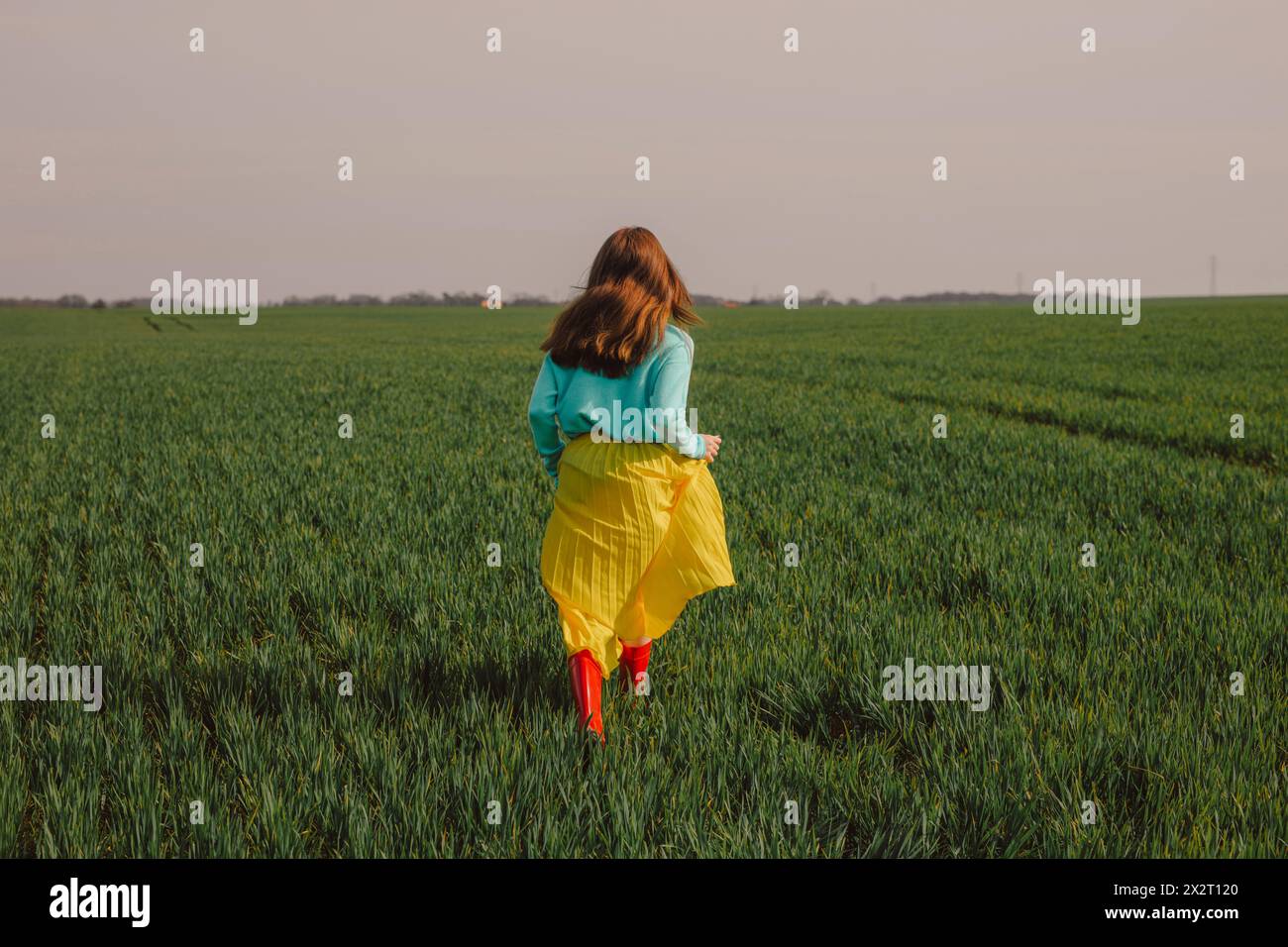 Giovane donna che indossa una gonna gialla e corre sul campo di grano verde sotto il cielo Foto Stock