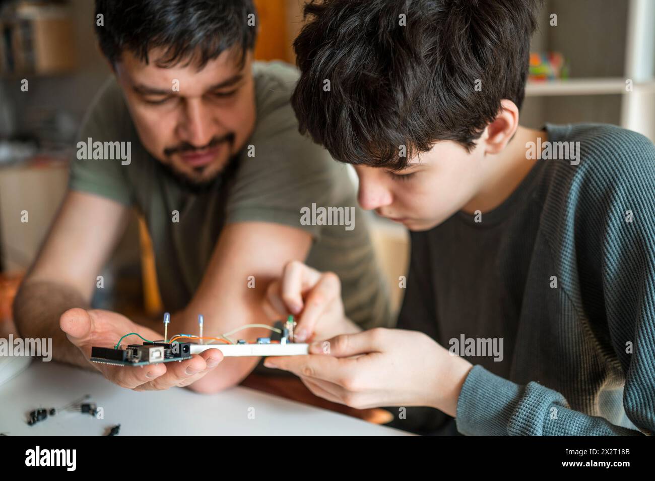 Padre che aiuta il figlio a riparare le apparecchiature elettriche a casa Foto Stock