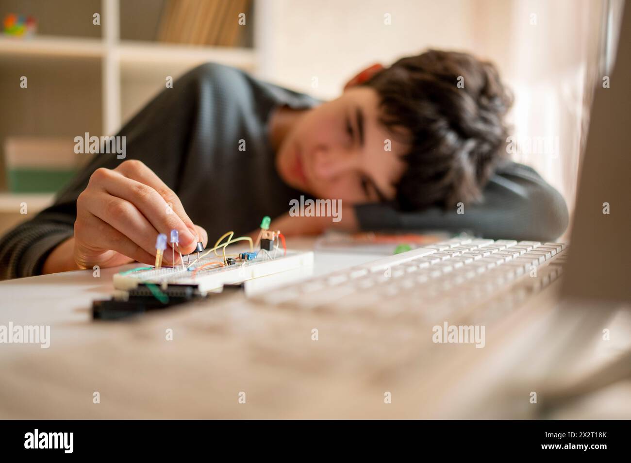 Ragazzo che regola il microcontrollore elettrico vicino alla tastiera di casa Foto Stock