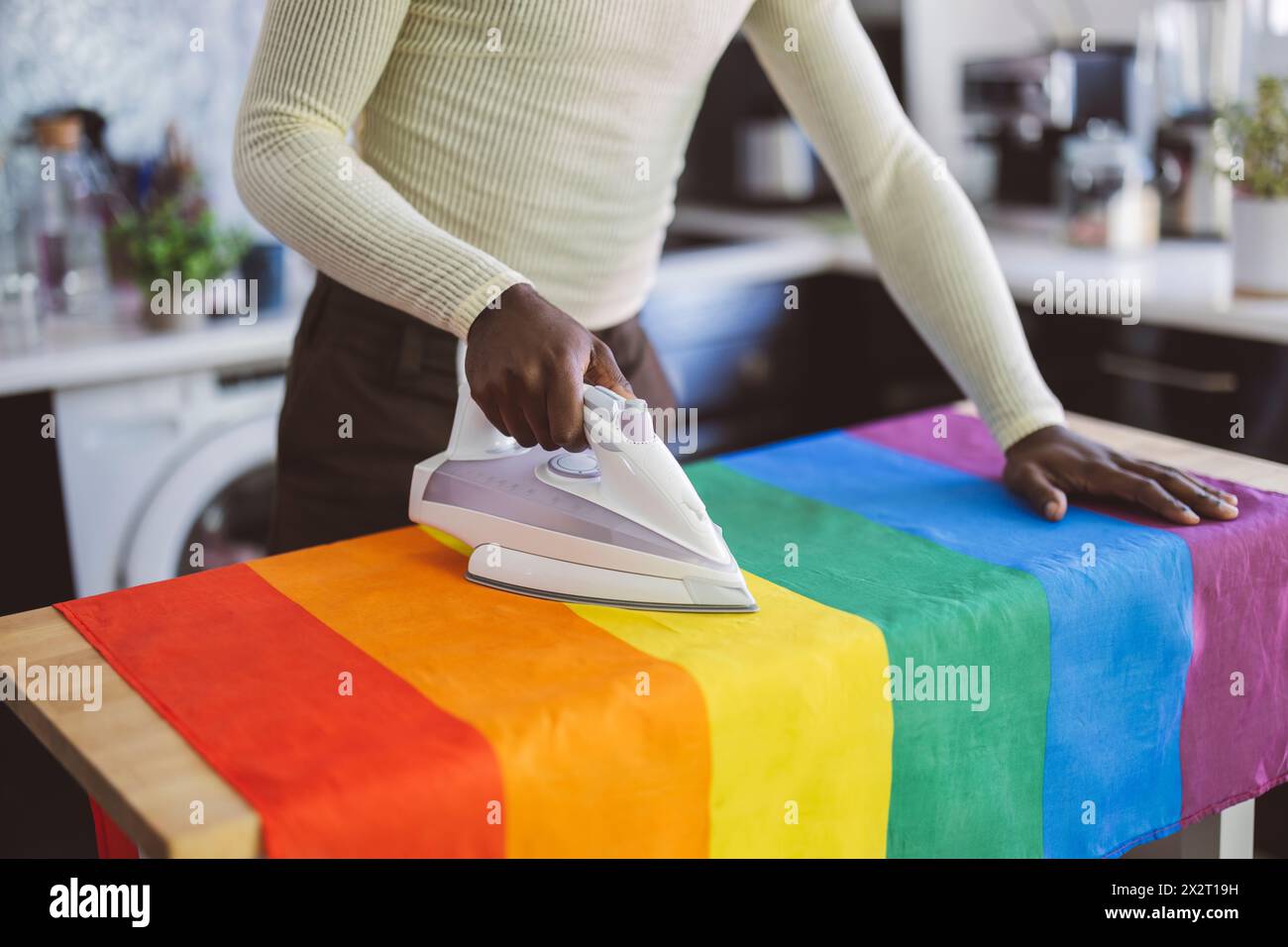 Persona non binaria che stirava bandiera arcobaleno a casa Foto Stock