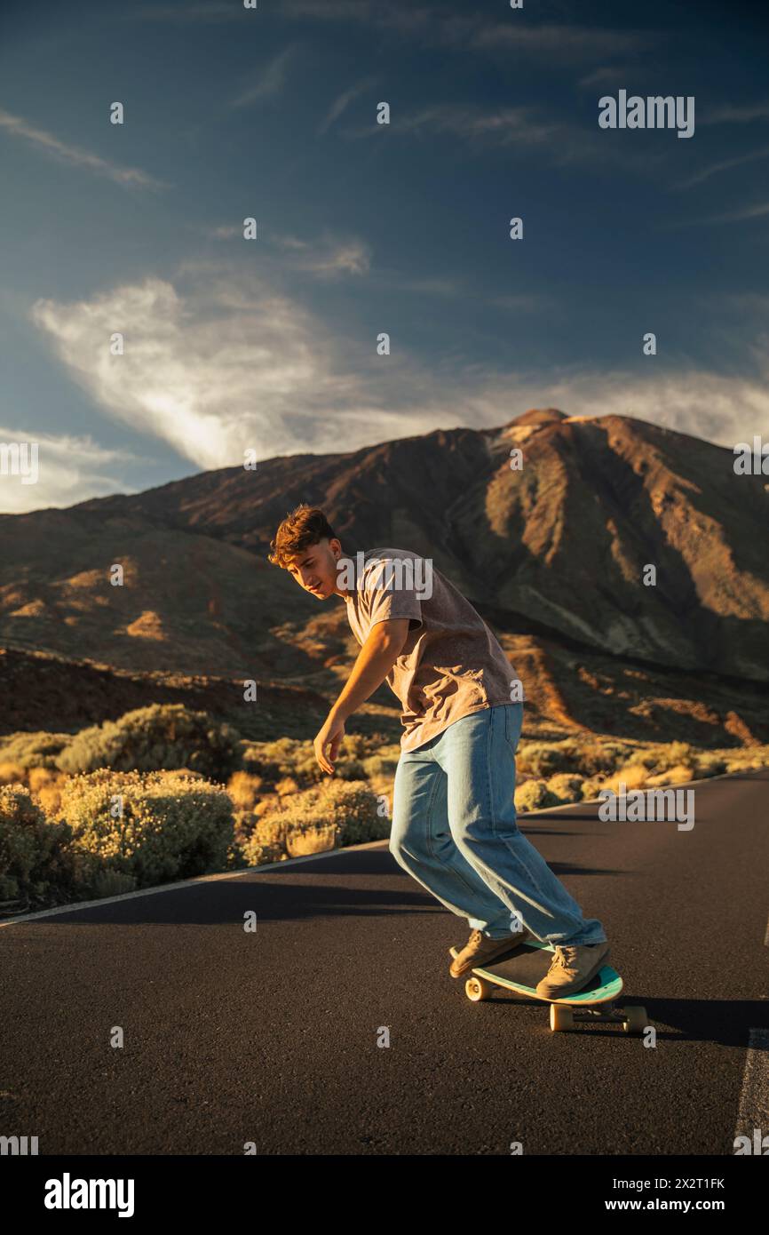 Skateboard uomo spensierato su una strada di montagna di fronte al monte Teide Foto Stock