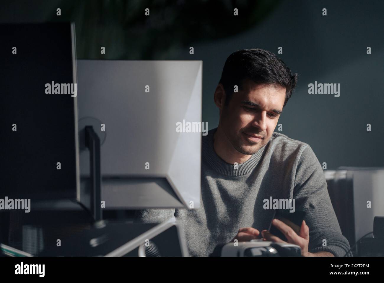 Uomo d'affari che utilizza un telefono cellulare vicino a un PC desktop in ufficio Foto Stock