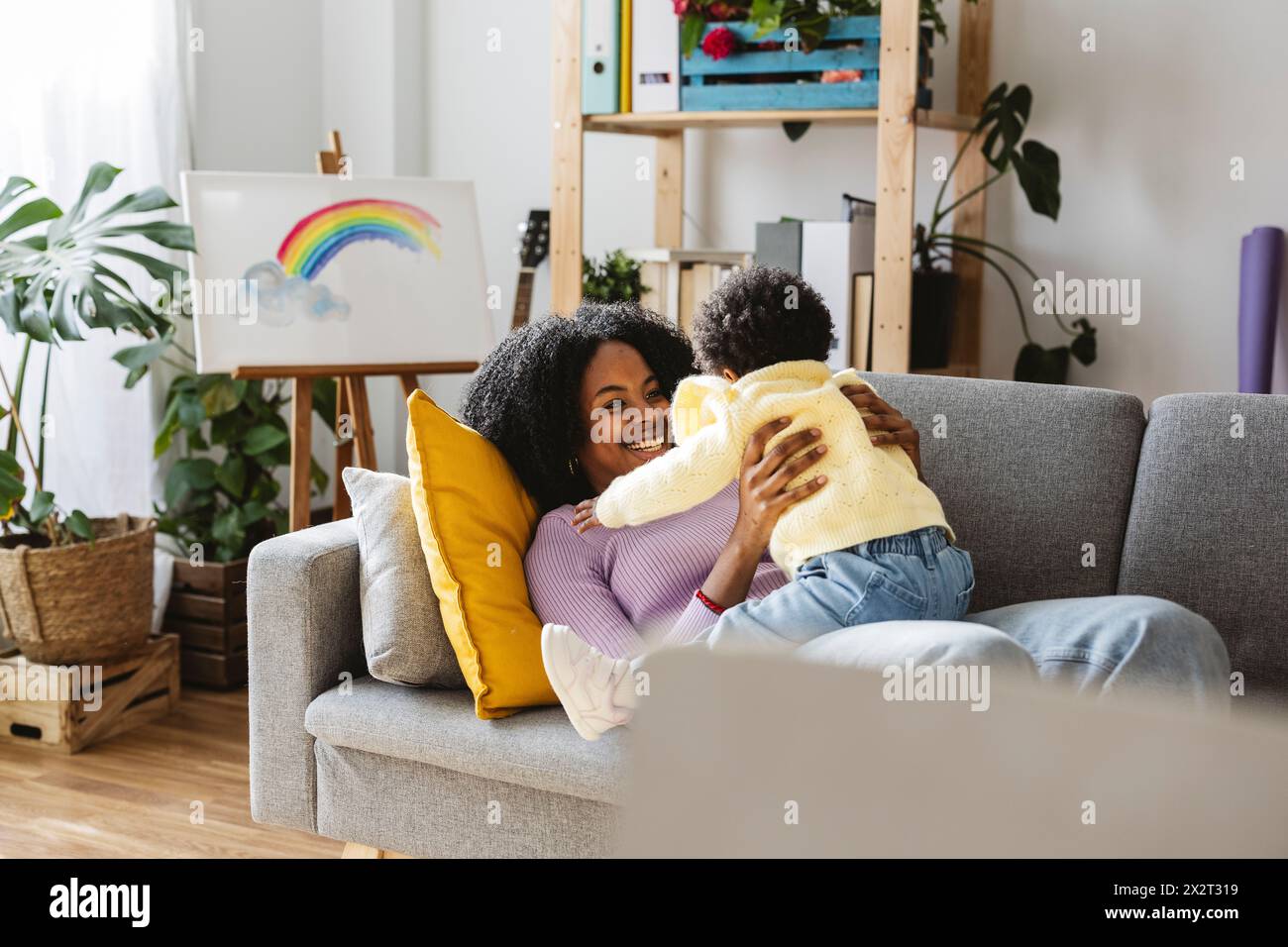 Madre single felice sdraiata sul divano che gioca con la bambina nel soggiorno di casa Foto Stock