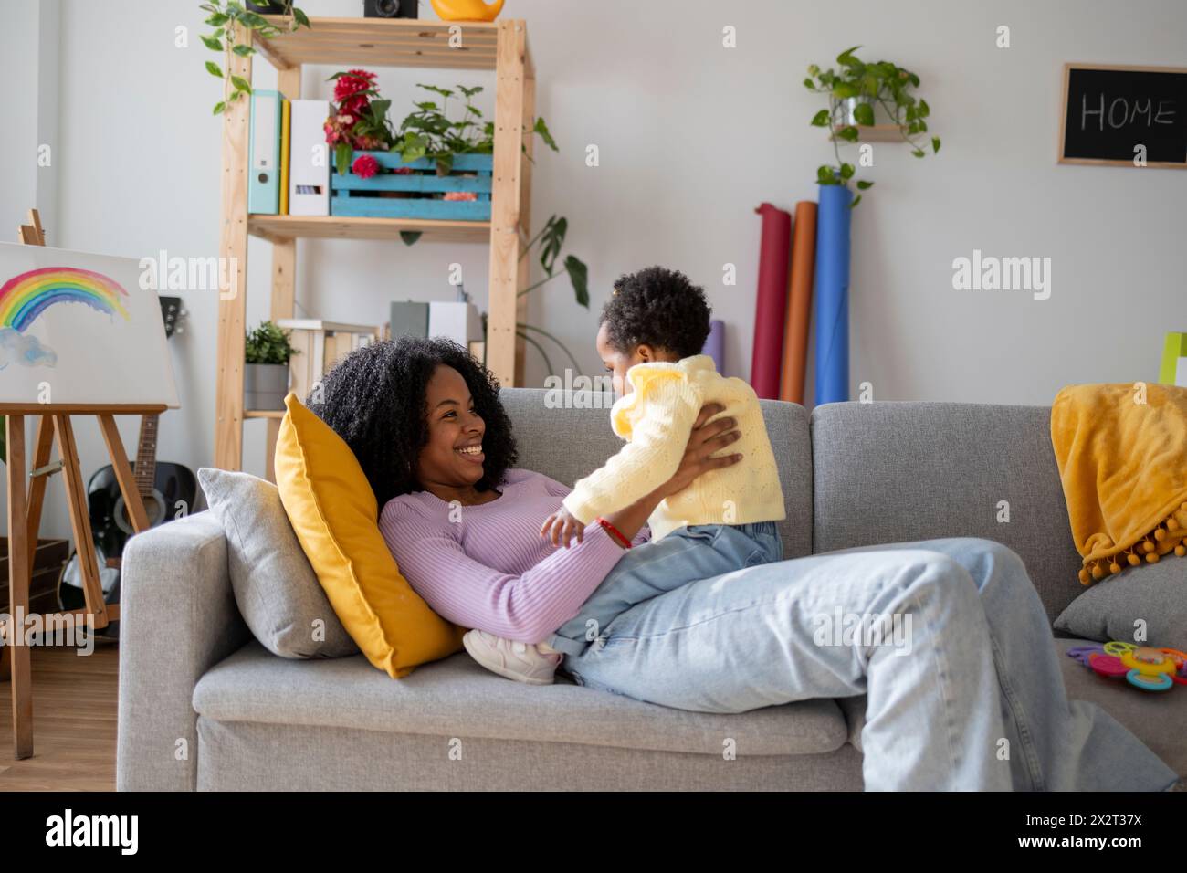 Mamma single sorridente sdraiata sul divano che gioca con la bambina nel soggiorno di casa Foto Stock