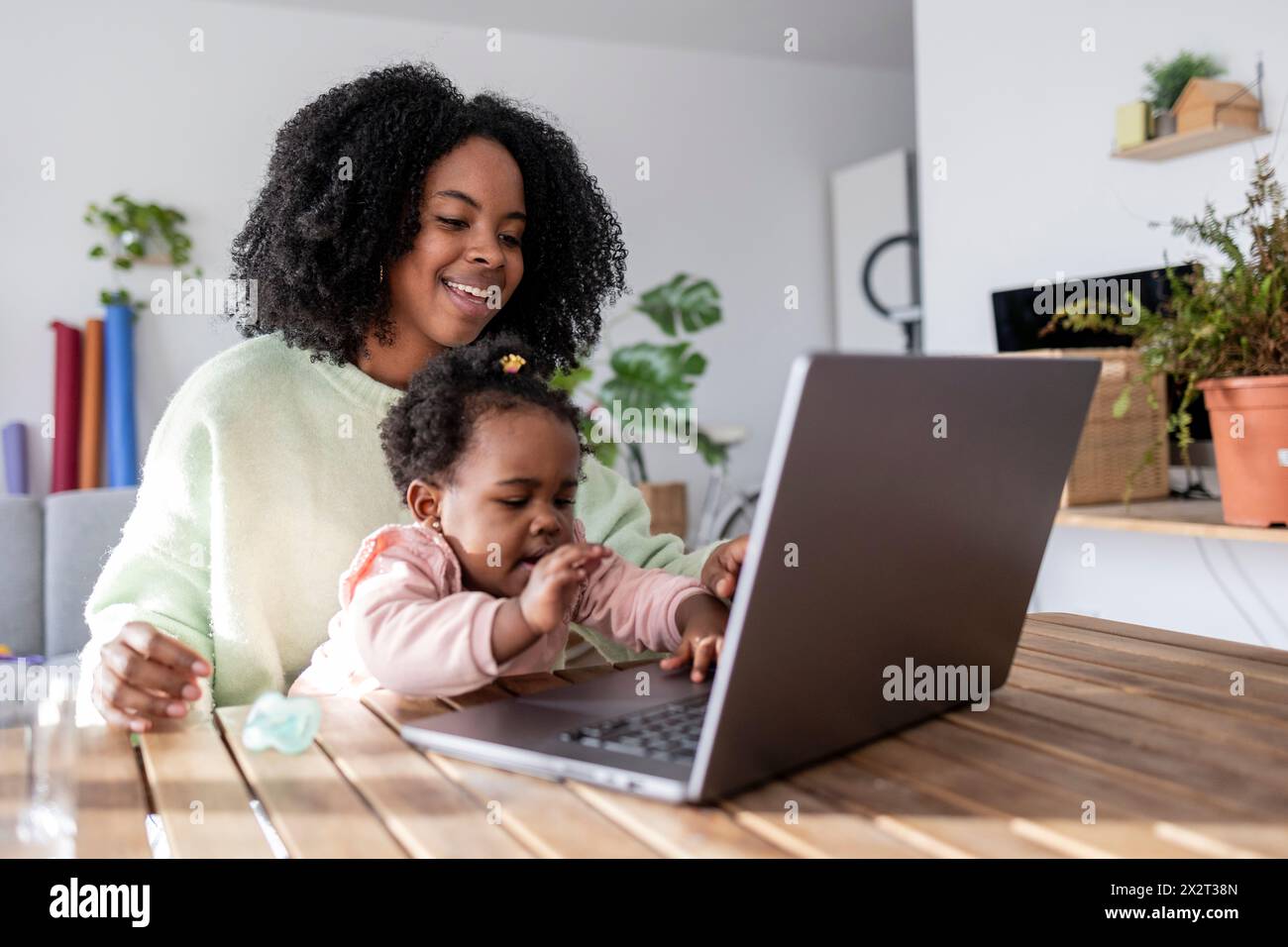Madre felice che lavora guardando la figlia che gioca con il portatile a casa Foto Stock