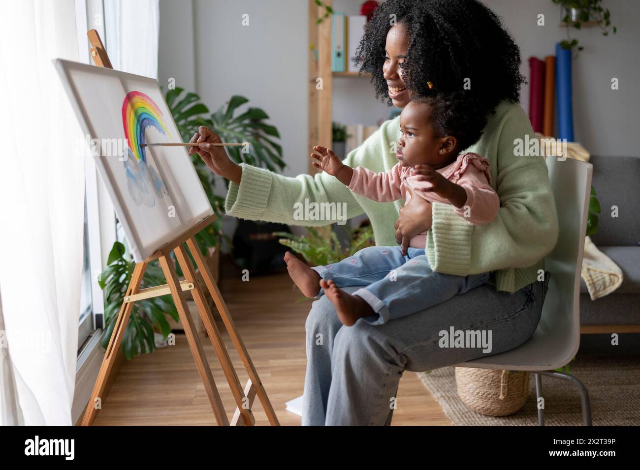 Madre single sorridente che dipinge l'arcobaleno con la figlia a casa Foto Stock