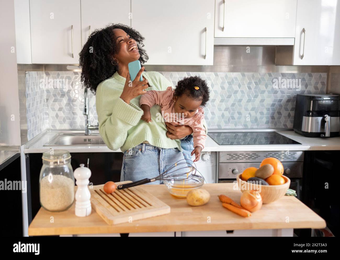 Allegra madre single che porta la figlia che parla al telefono cellulare in cucina a casa Foto Stock