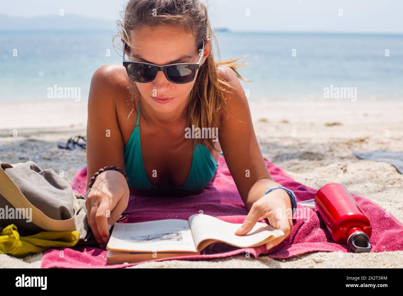 Donna con occhiali da sole che legge un libro in spiaggia Foto Stock