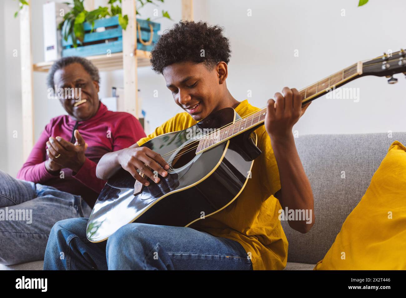 Ragazzo sorridente che suona la chitarra di nonno sul divano di casa Foto Stock