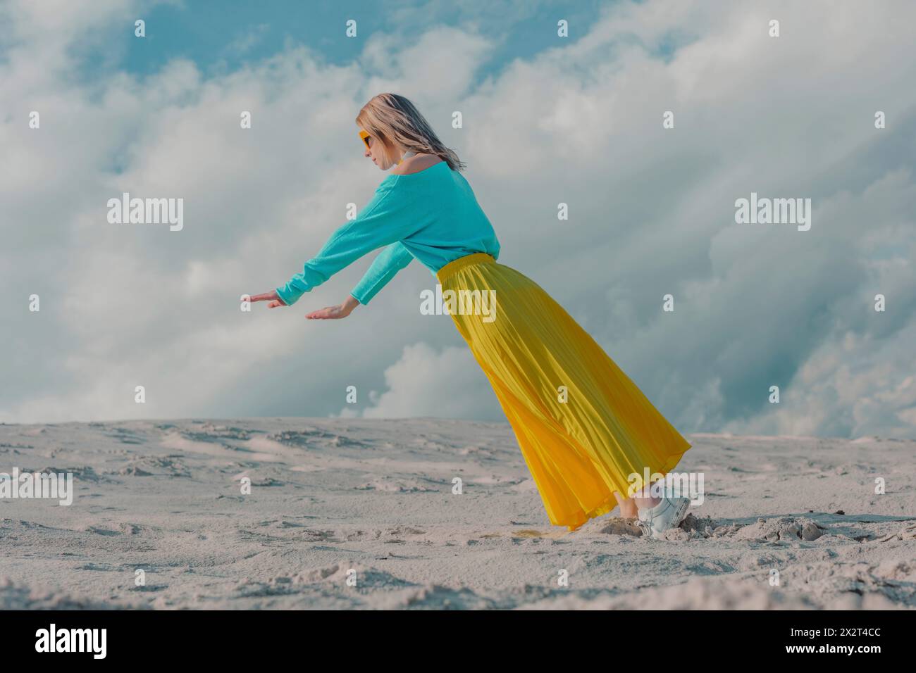 Donna che indossa una gonna gialla in equilibrio sui piedi sotto il cielo nuvoloso Foto Stock