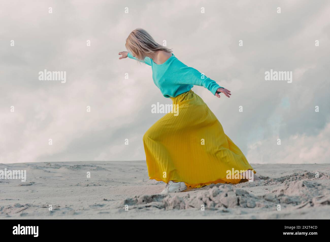 Donna che indossa una gonna gialla e cammina sulle dune di sabbia sotto il cielo nuvoloso Foto Stock