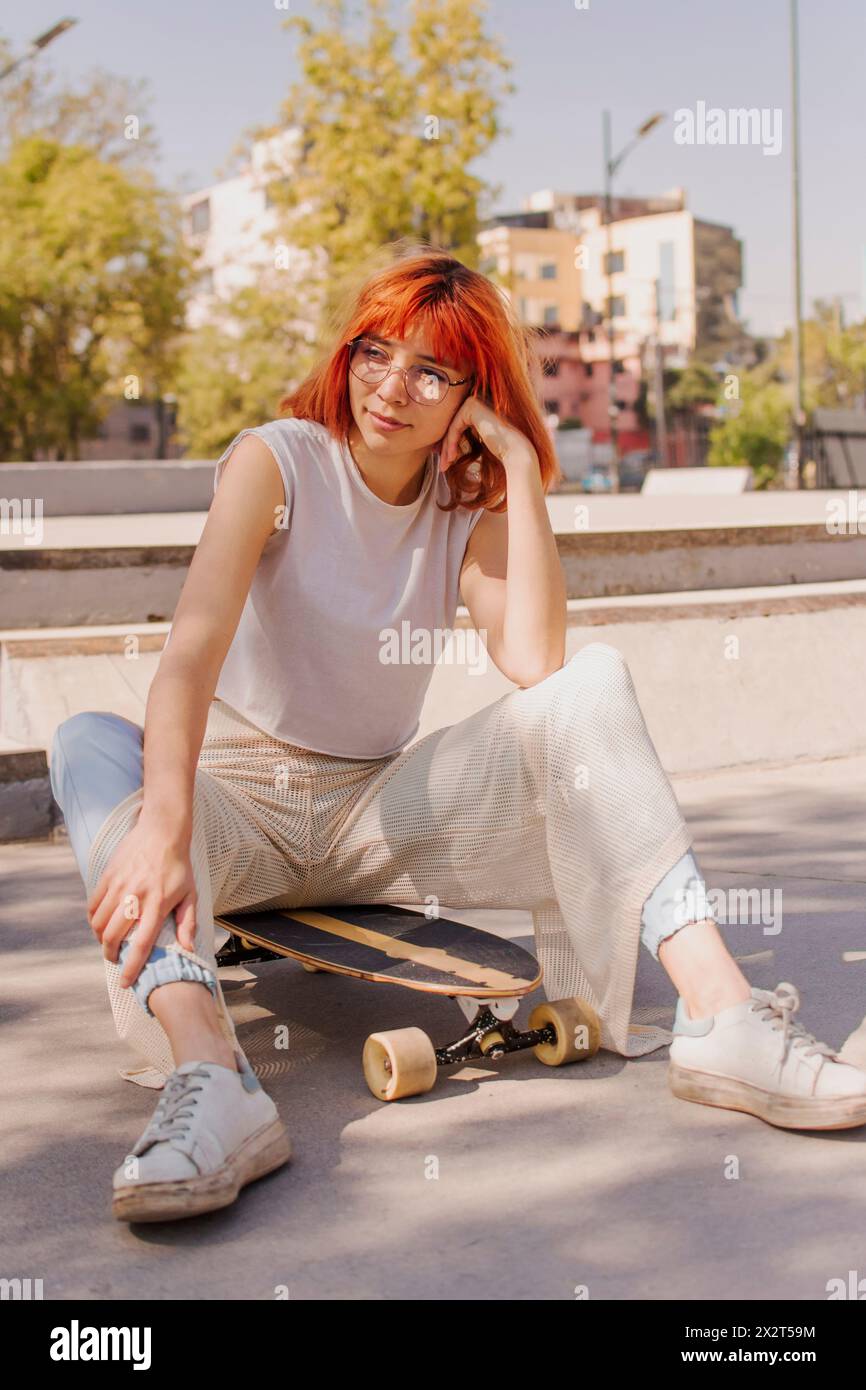 Donna rossa seduta sullo skateboard al parco Foto Stock