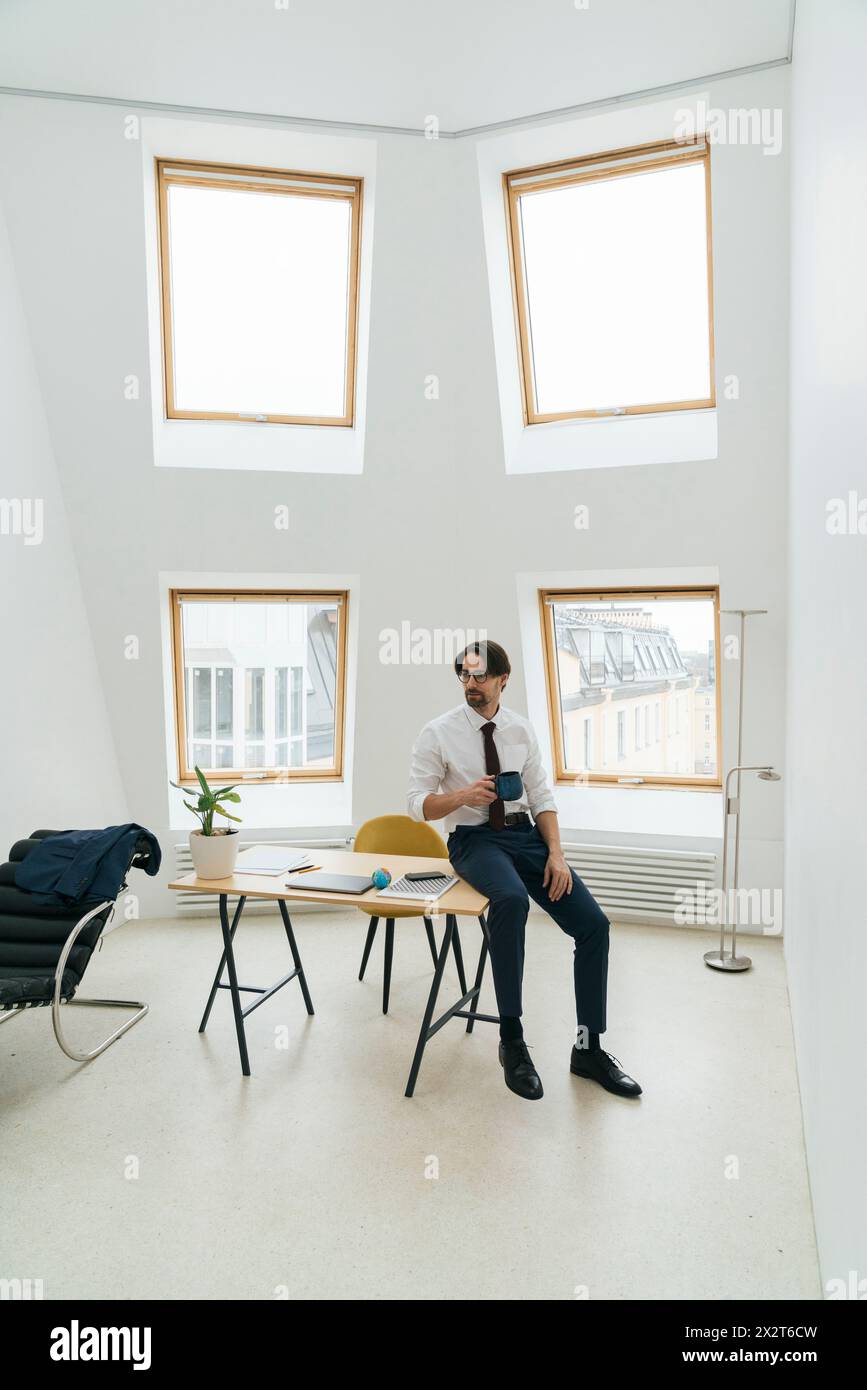 Uomo d'affari con tazza di caffè seduto alla scrivania in un ufficio minimalista Foto Stock