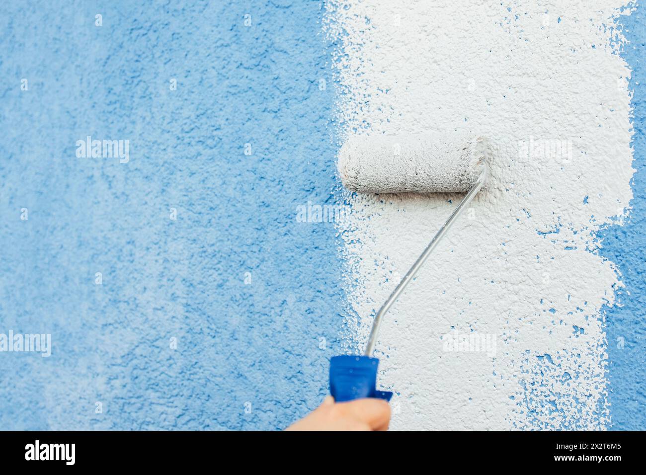 Mano di ragazza che dipinge il colore bianco sulla parete usando il rullo Foto Stock