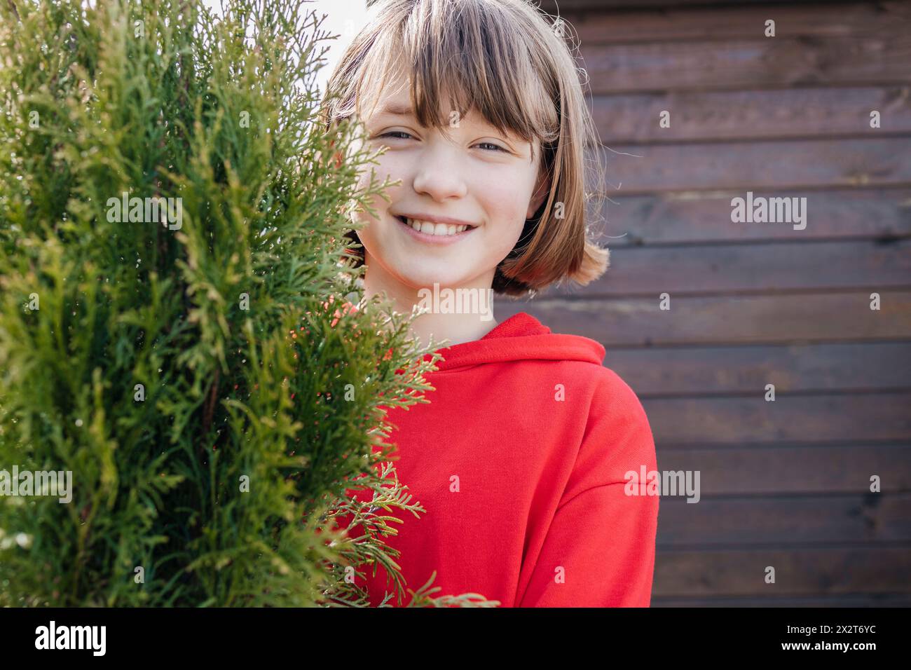 Ragazza sorridente con bangs marroni dietro la pianta Thuja Foto Stock