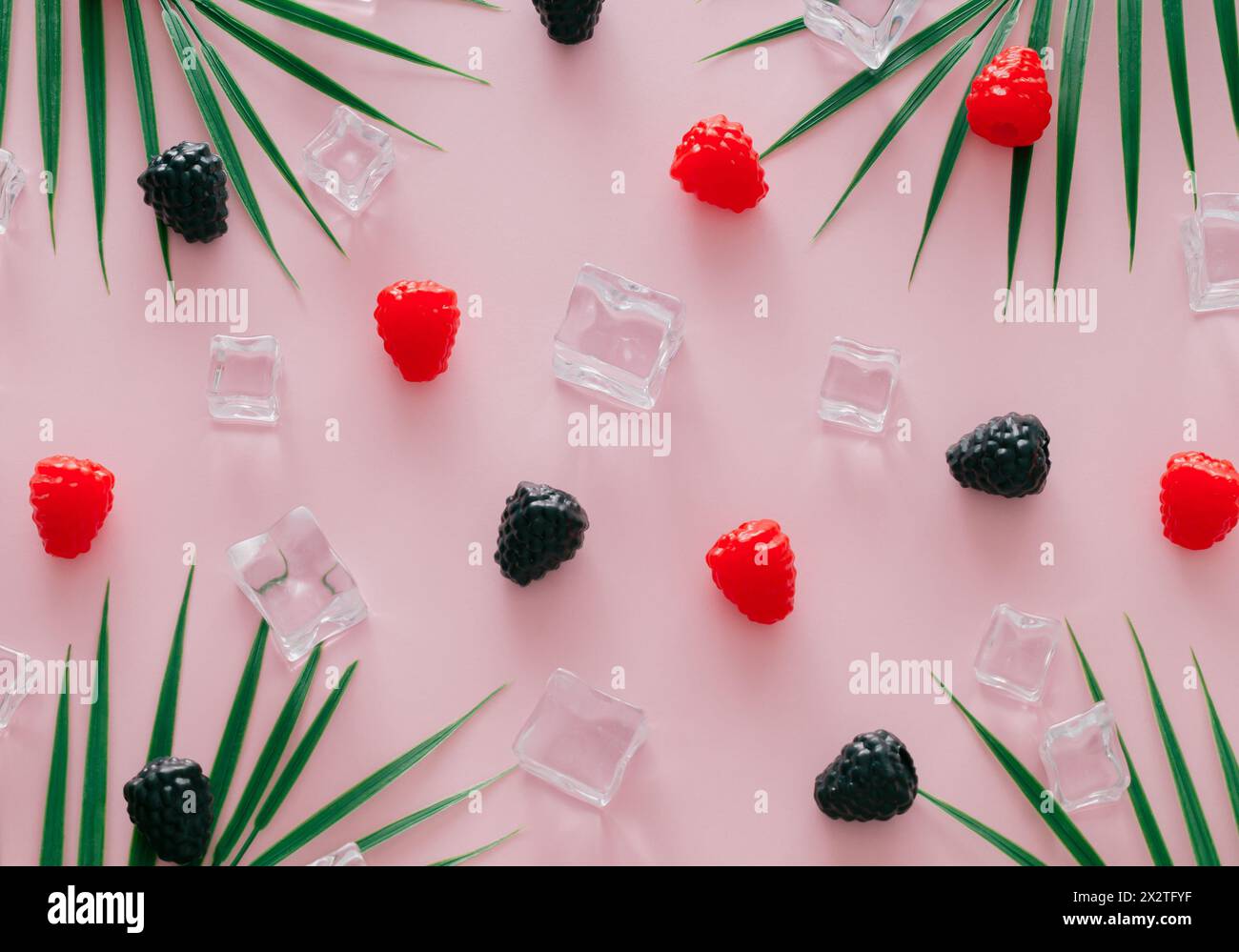 Fantasia estiva con lamponi, more, foglie di palma tropicale verde e cubetti di ghiaccio su sfondo rosa chiaro. Concetto minimale di frutta. Foto Stock