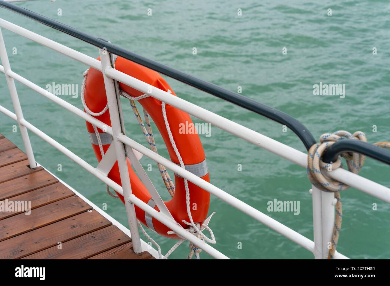 Un giubbotto salvagente arancione sulla ringhiera di una barca sull'acqua Foto Stock