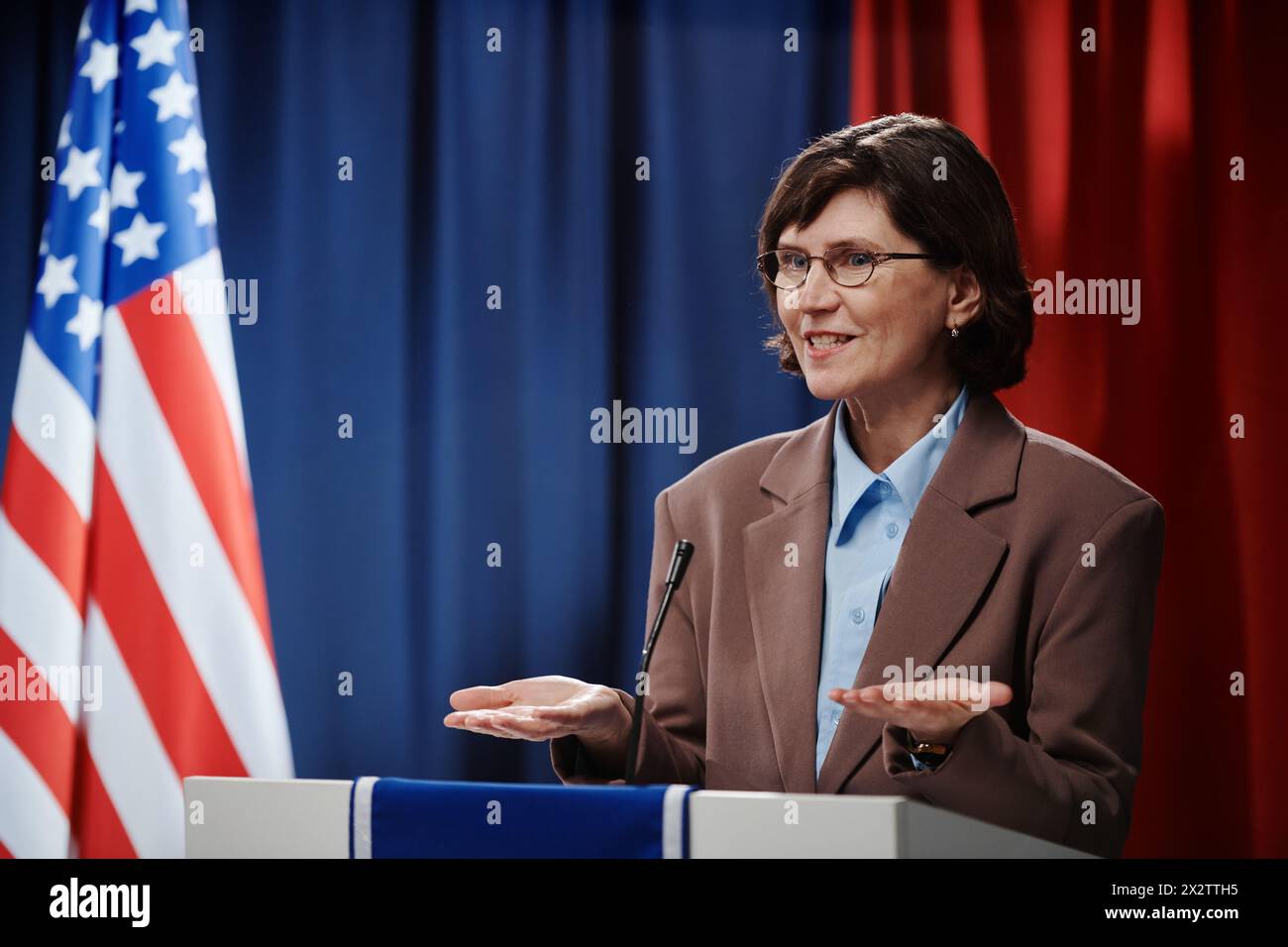 Vice o ministro donna matura che apre le palme e guarda l'elettorato mentre spiega i passi dello sviluppo economico Foto Stock