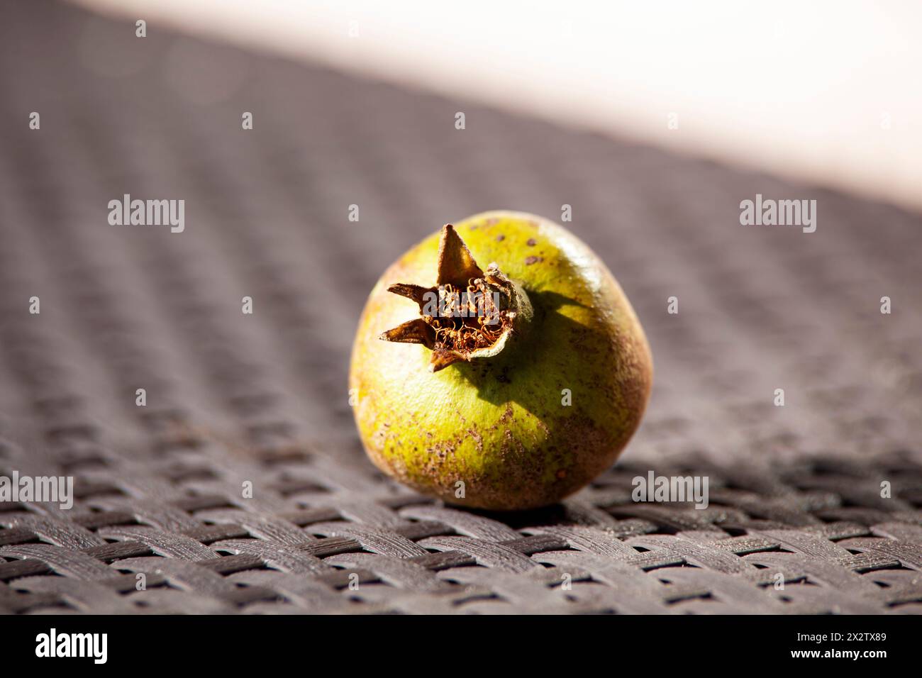 Melograno verde acuto su un tavolo marrone vimini alla luce del sole. Un frutto autunnale. Cibo sano. Orizzontale Foto Stock