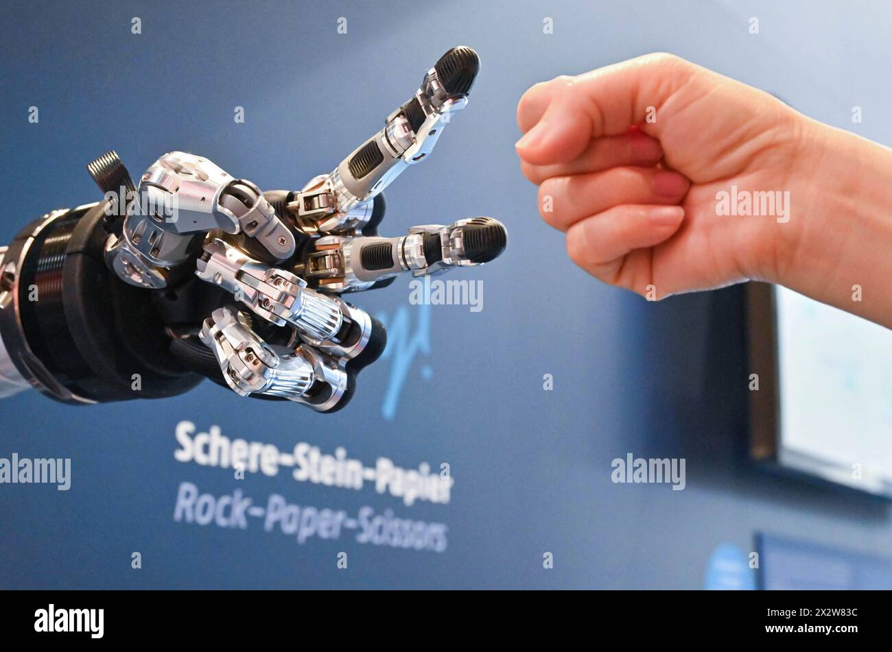 Hannover, Germania. 23 aprile 2024. Un visitatore gioca a forbici da carta rock con un robot intelligente alla Hannover Messe di Hannover, Germania, il 23 aprile 2024. La fiera Hannover Messe 2024, la fiera industriale leader in Germania, ha dato il via lunedì con una chiara enfasi sulla produzione a emissioni zero e sulle celle a combustibile a idrogeno. Crediti: Ren Pengfei/Xinhua/Alamy Live News Foto Stock