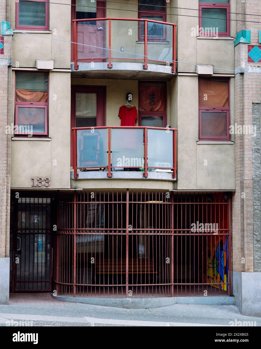 Una foto di un abito rosso o di una maglietta appesa su un appendiabiti alla luce di un piccolo balcone di un condominio dall'aspetto trascurato. Foto Stock